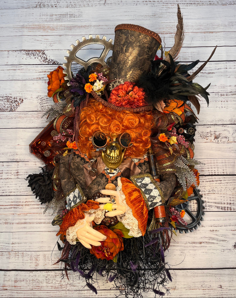 Steampunk gothic wall art featuring a skull with goggles, a tall top hat, gears, feathers, flowers, and a small doll's hands, arranged on a whitewashed wood plank background.